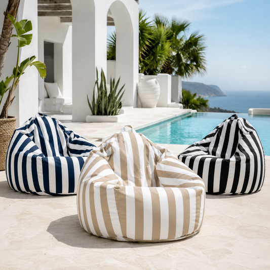 Three oversized striped bean bag chairs arranged around a poolside patio. The front chair is beige and white vertically striped, while the two side chairs are navy and white striped on the left and black and white striped on the right.
