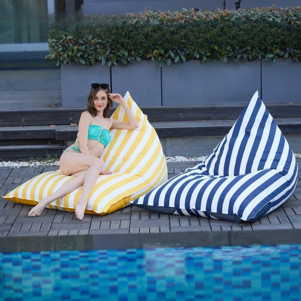 Aussie Waterproof Floating Triangle Beanbag Covers 100x140 in yellow and white vertical stripe and blue and white vertical stripe, displayed poolside with a person seated on one beanbag.