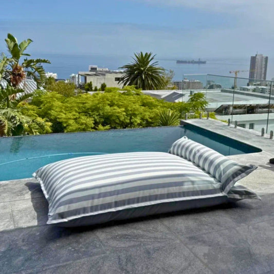 Product image of the Big Bertha floating beanbag lounger cover in light grey and white stripe, displayed on an outdoor poolside deck.