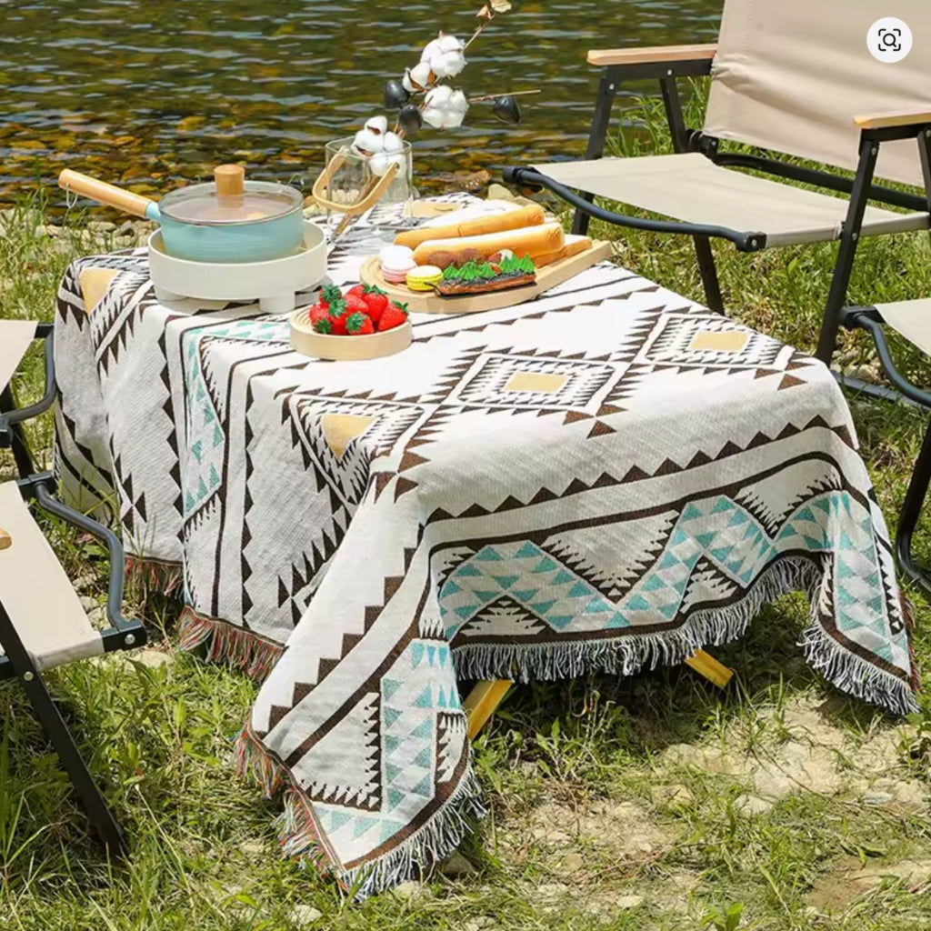 Lifestyle image of the Coastal Picnic Rug in ta geo pattern displayed ontablewith picnic food and accessories.