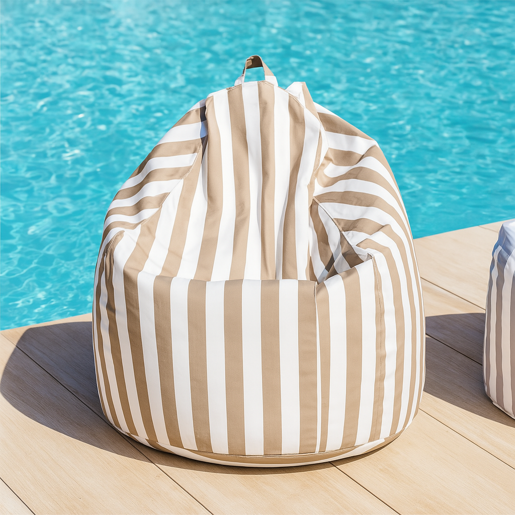 A beige and white striped teardrop bean bag cover styled poolside on a wooden deck with a turquoise blue pool backdrop