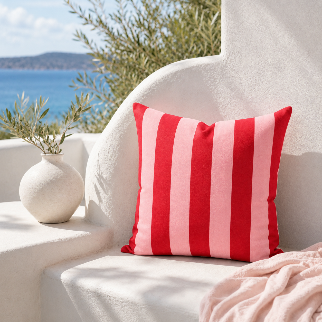 Pink and red striped weatherproof outdoor cushion cover styled on a sunny coastal terrace