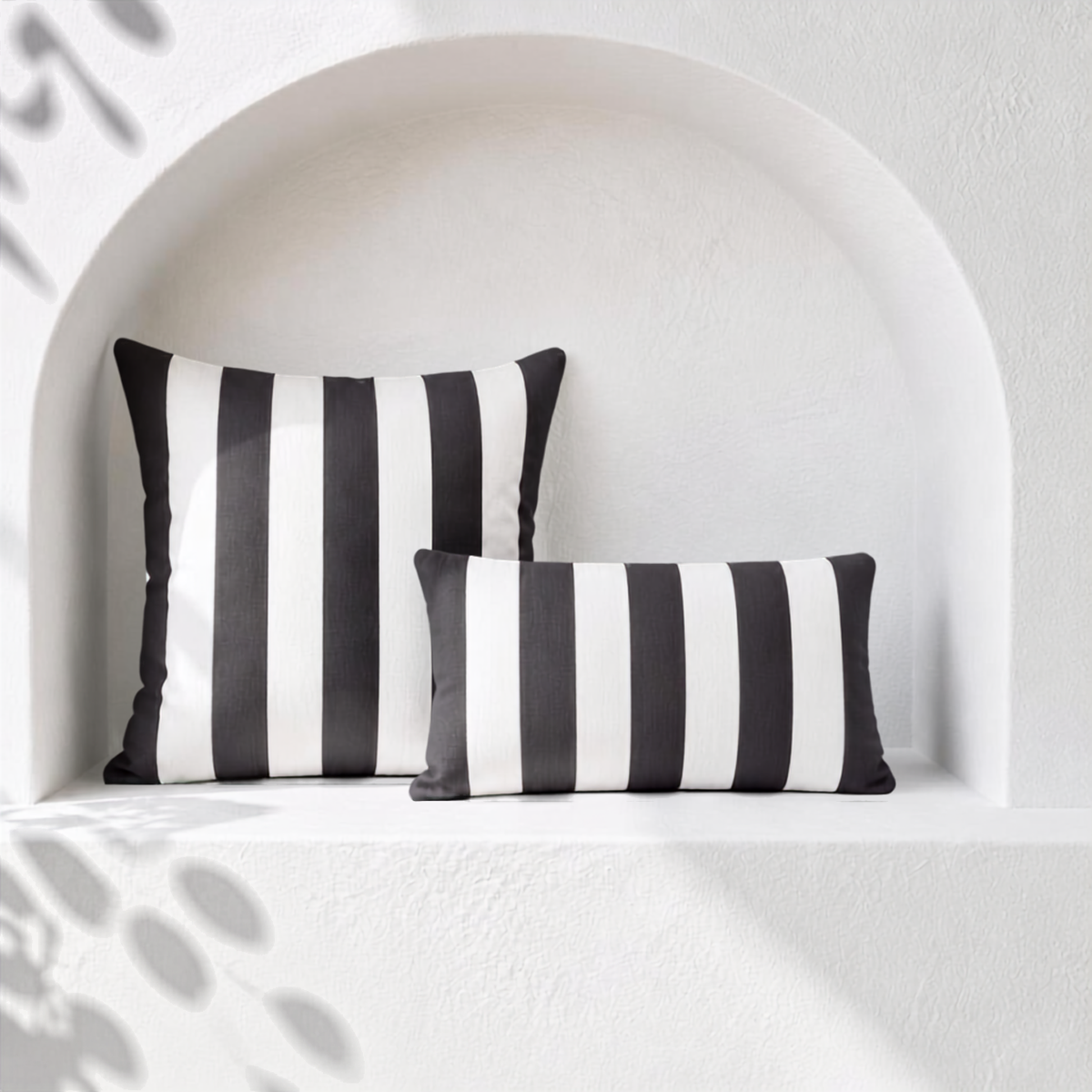 Two dark grey and white striped weatherproof outdoor cushion covers styled in a white arched Santorini niche