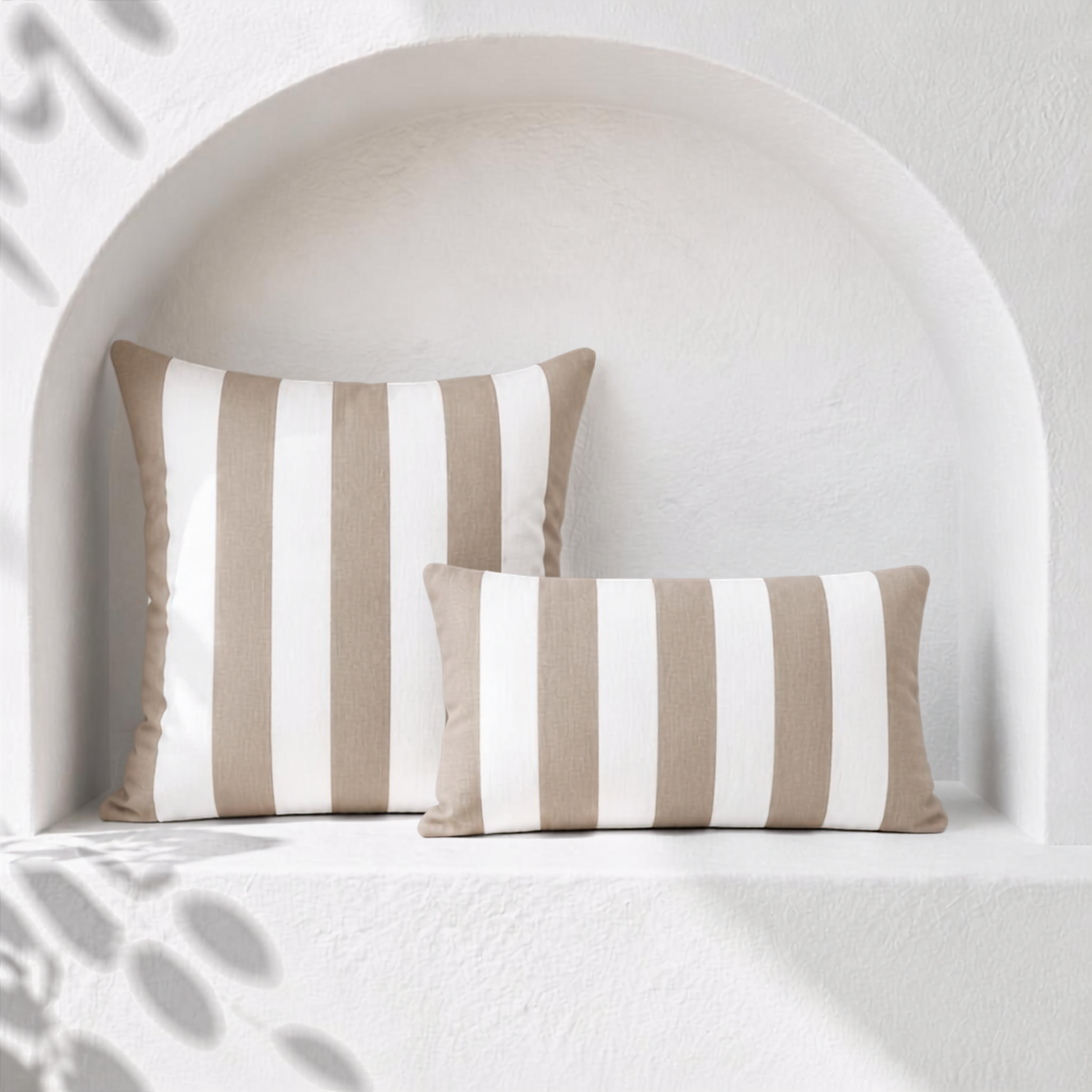 Two khaki beige and white striped weatherproof outdoor cushion covers styled in a white arched Santorini niche