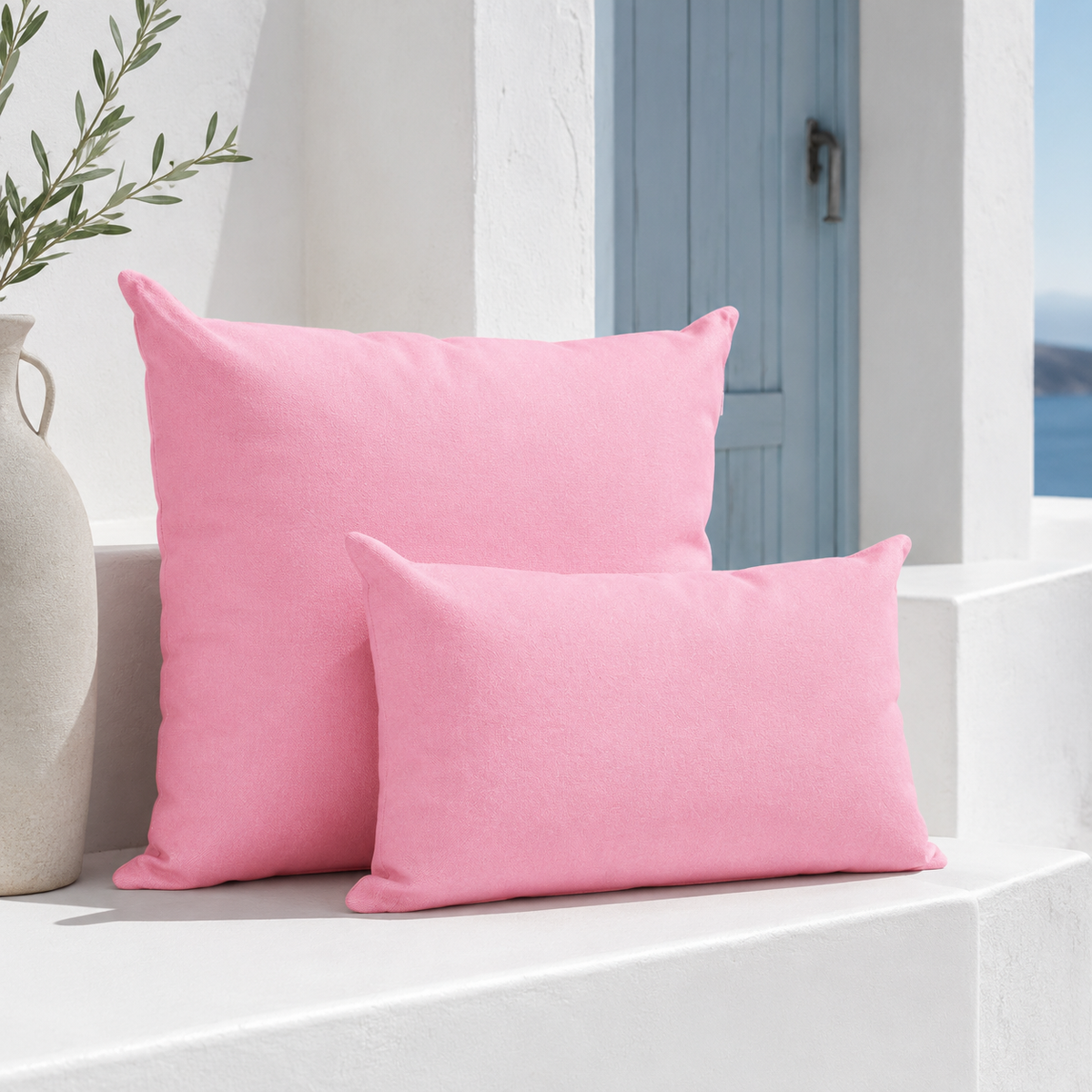 Two pink weatherproof outdoor cushion covers styled in a white Santorini niche