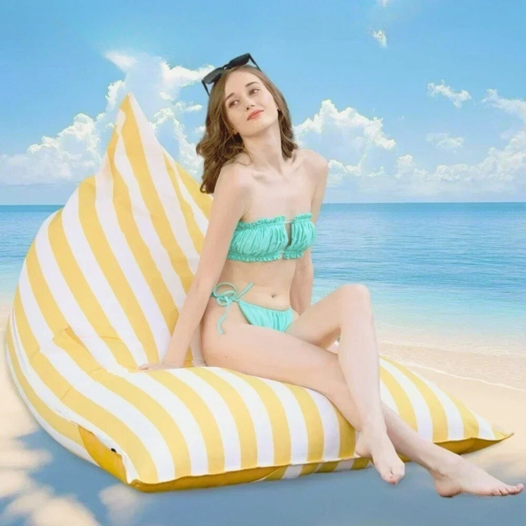 Aussie Waterproof Floating Triangle Beanbag Cover 100x140 in yellow and white vertical stripe, shown on the beach with a person relaxing on top.