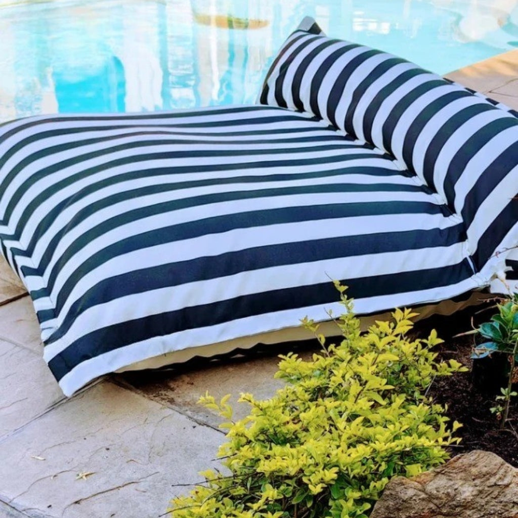 Lifestyle image of the Big Bertha double floating beanbag lounger cover in black and white stripe, displayed on a poolside deck to show size and outdoor use.