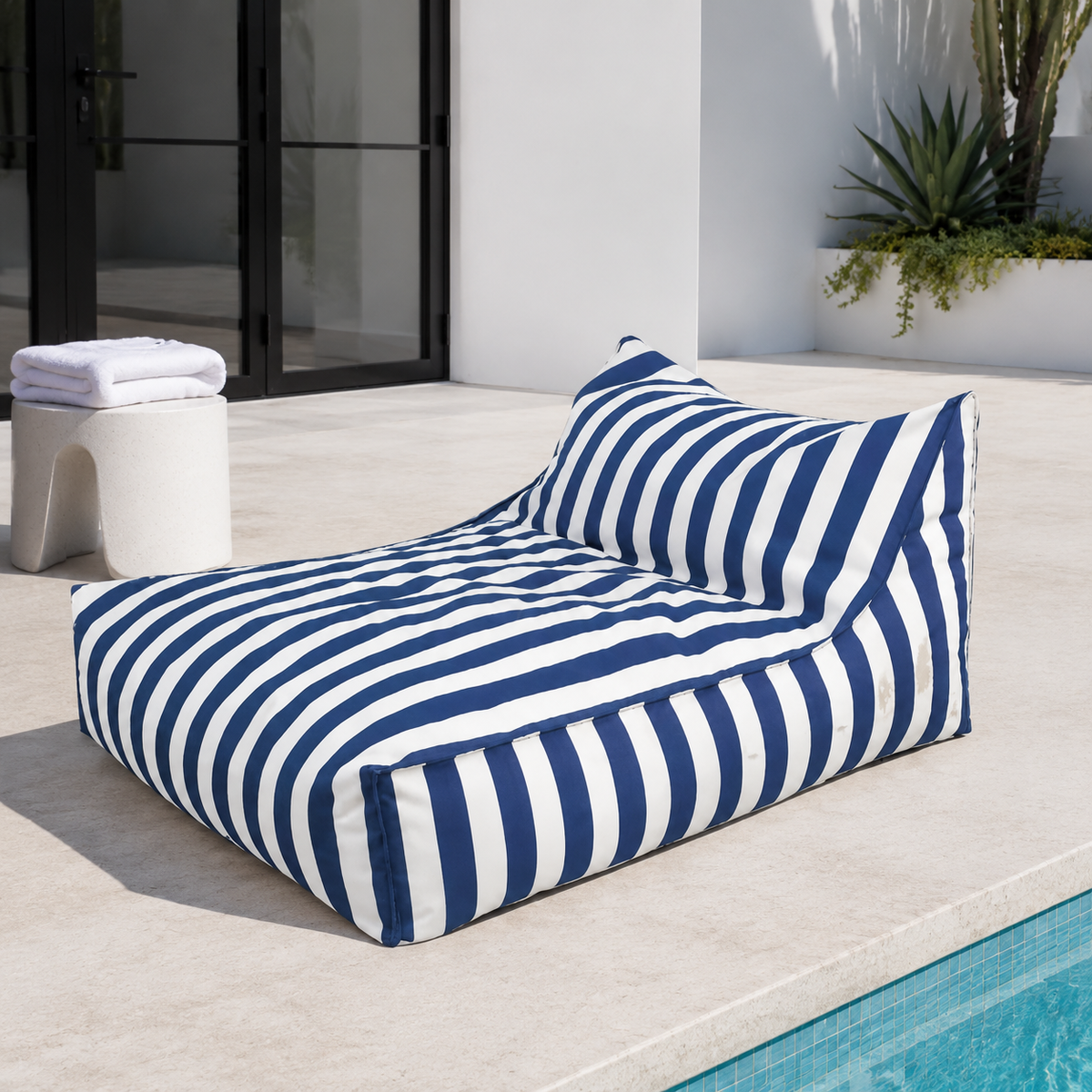 Blue and white striped Big Chill weatherproof beanbag lounger beside a contemporary pool house with a folded white towel.