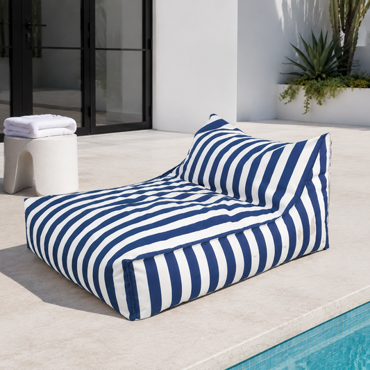 Blue and white striped Big Chill weatherproof beanbag lounger beside a contemporary pool house with a folded white towel.