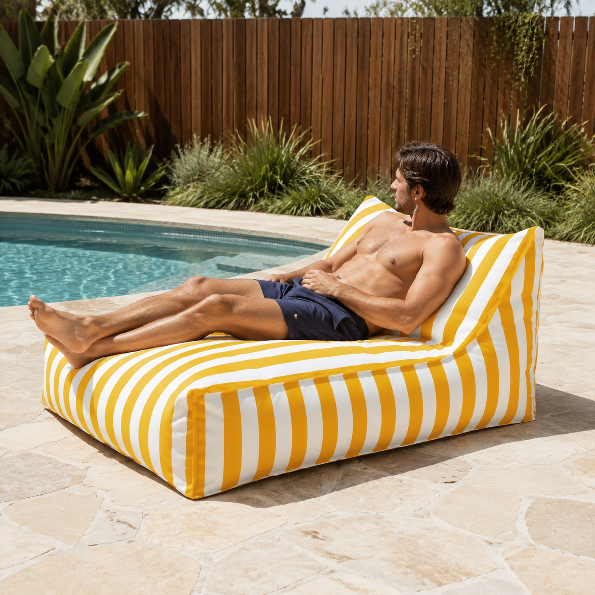 Yellow and white striped Big Chill weatherproof beanbag lounger with a man relaxing beside an Australian backyard pool.