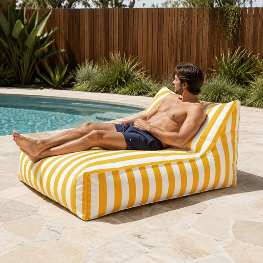 Yellow and white striped Big Chill weatherproof beanbag lounger with a man relaxing beside an Australian backyard pool.