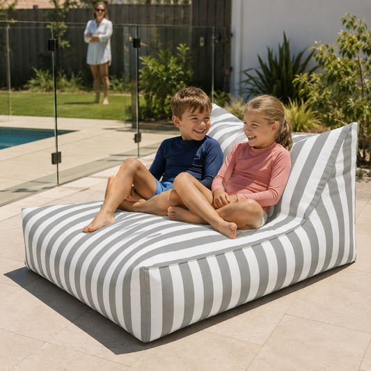 Light grey and white striped Big Chill weatherproof beanbag lounger with two children beside a fenced Australian backyard pool.