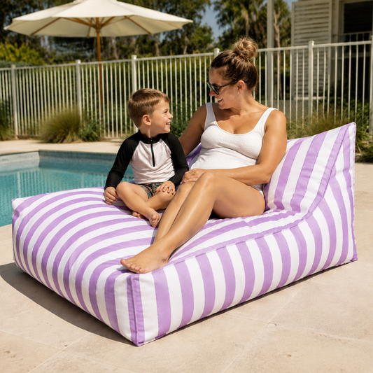 Purple and white striped Big Chill weatherproof beanbag lounger with a mother and child beside a fenced Australian backyard pool.