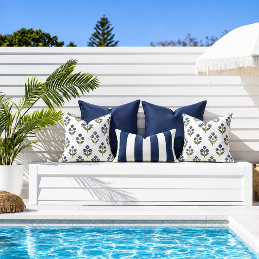Fleur Navy water-resistant outdoor sofa cushion cover set with two navy 50 x 50 cushions, two blue and green floral 45 x 45 cushions and a navy white striped 30 x 50 lumbar cushion beside a pool