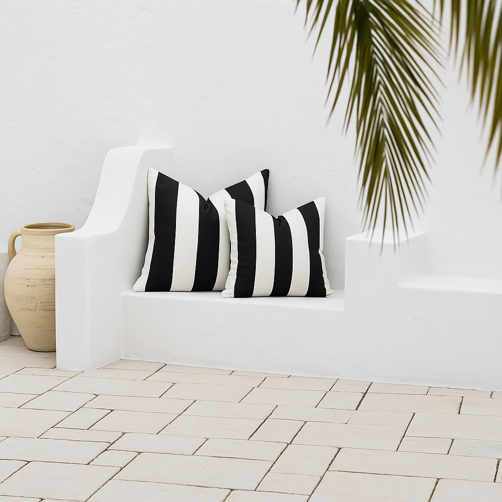 Black and white striped pillows, square design,  on a white outdoor sofa with a plant and vase in the background.