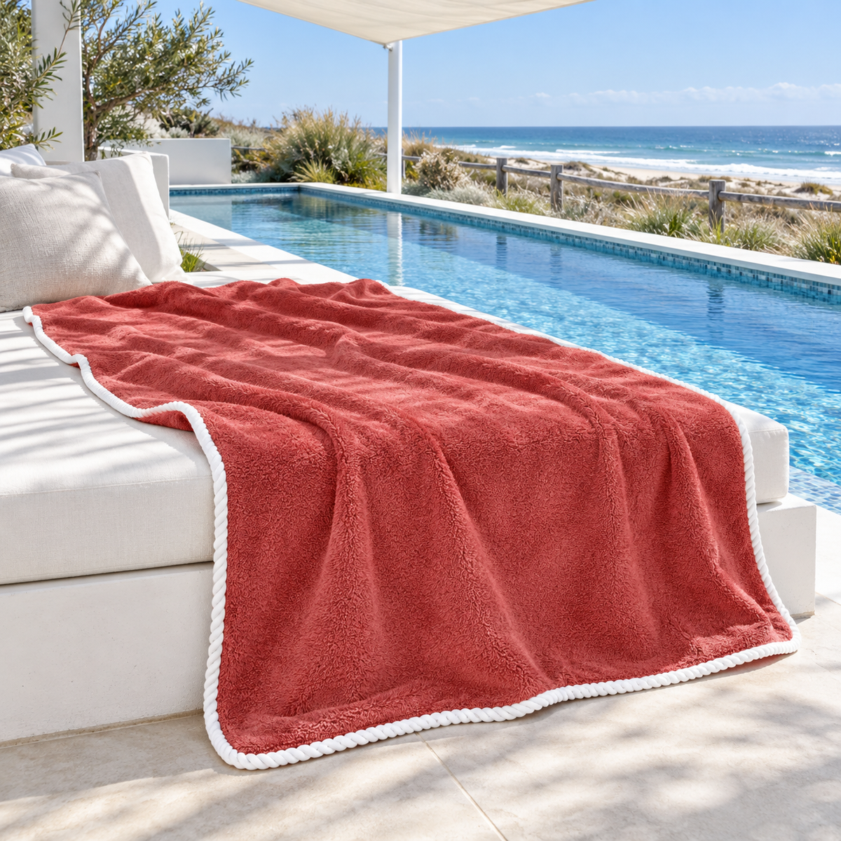Noosa extra large coral towel with white piped edging spread across a poolside daybed overlooking Australian coastal dunes.