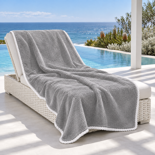 Noosa extra large grey towel with white piped edging draped over a white lounger beside an Australian coastal infinity pool.