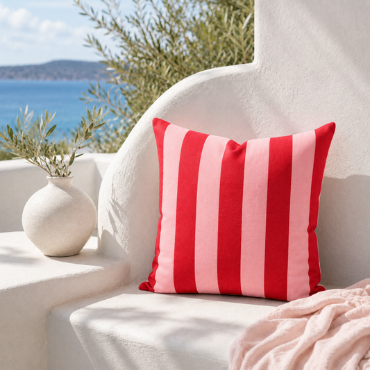 Pink and red striped weatherproof outdoor cushion cover styled on a sunny coastal terrace