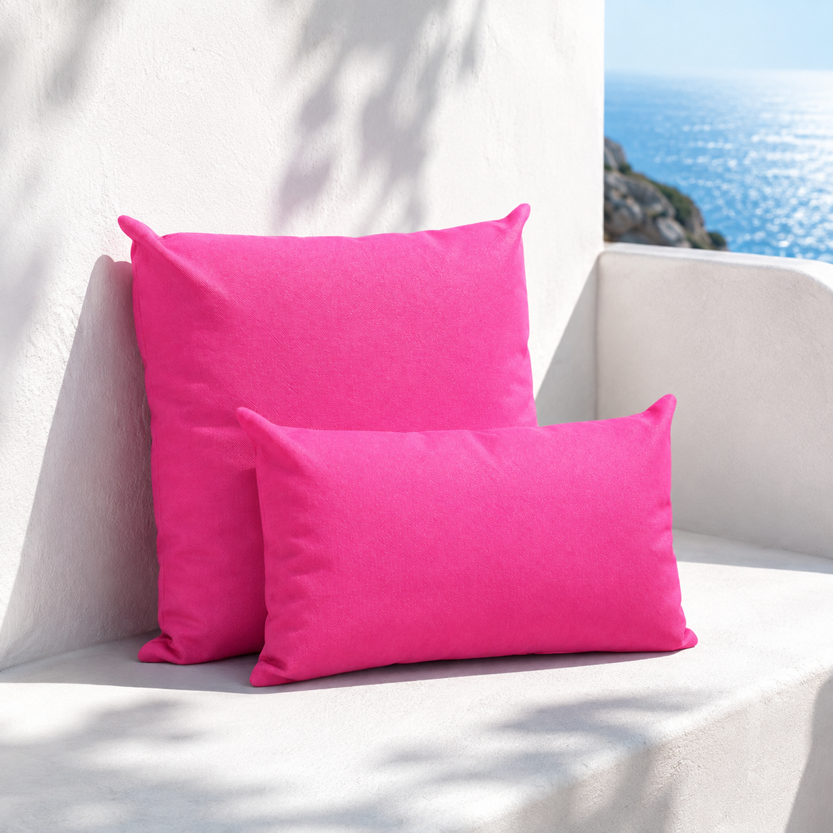 Santorini fuchsia weatherproof outdoor square and lumbar cushions styled in a white Mediterranean seating nook with sea view