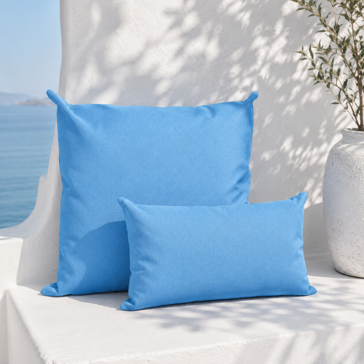 Santorini lake blue weatherproof outdoor square and lumbar cushions styled in a white Mediterranean seating nook with sea view
